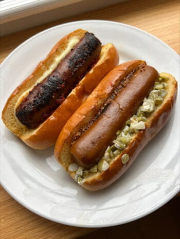 two hot dogs on buns with toppings on a plate